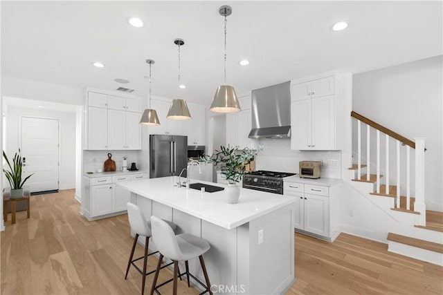 kitchen featuring a sink, light wood-type flooring, high end appliances, and wall chimney range hood