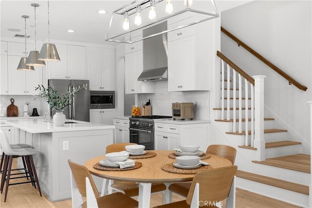 kitchen featuring tasteful backsplash, visible vents, light wood finished floors, wall chimney range hood, and stainless steel appliances