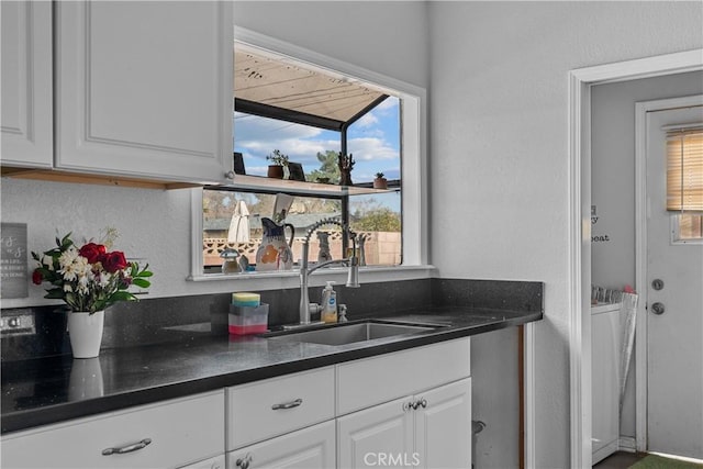 kitchen featuring plenty of natural light, white cabinets, a sink, and dark countertops