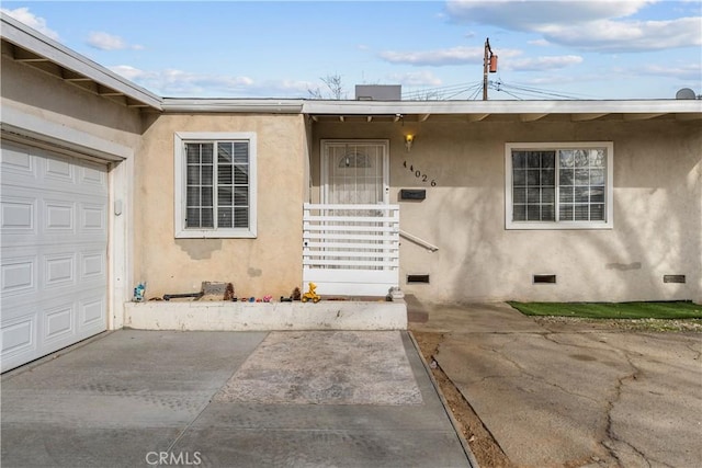 property entrance featuring a garage, driveway, crawl space, and stucco siding