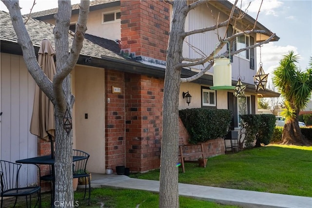 exterior space featuring a shingled roof, brick siding, a chimney, and a front lawn