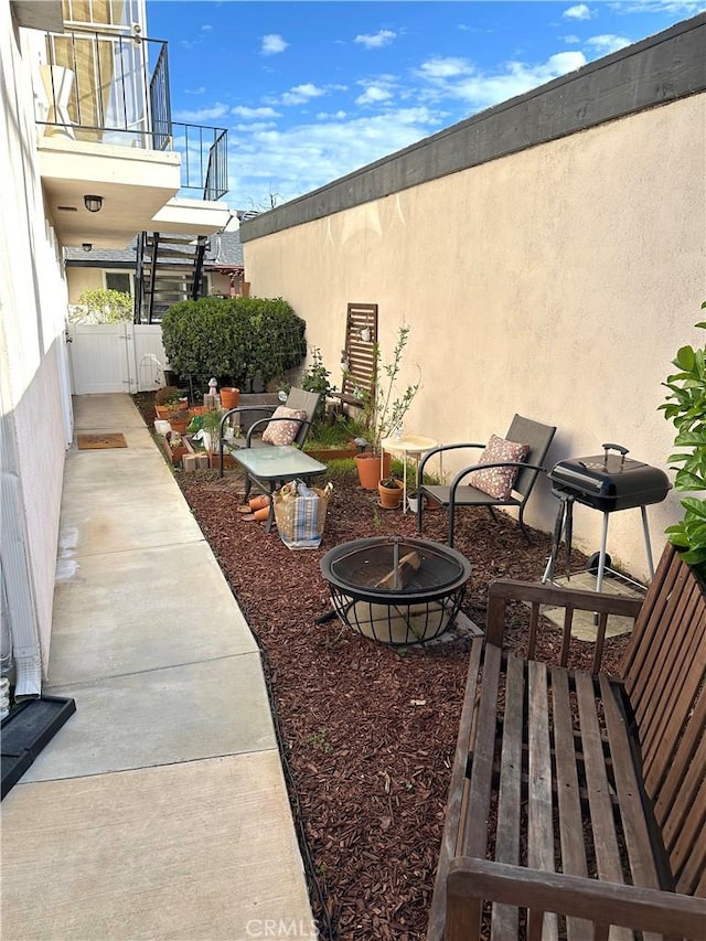 view of patio with a grill, fence, a fire pit, and a balcony