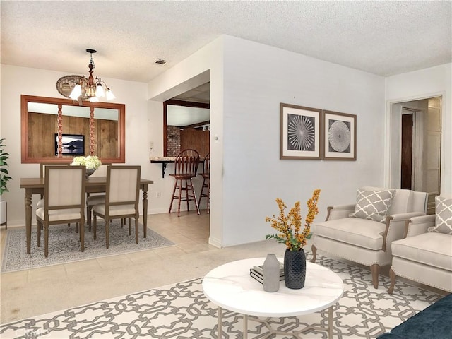 living room with a textured ceiling, baseboards, visible vents, and a chandelier