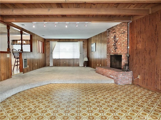 unfurnished living room with wooden walls, beamed ceiling, carpet flooring, a fireplace, and rail lighting