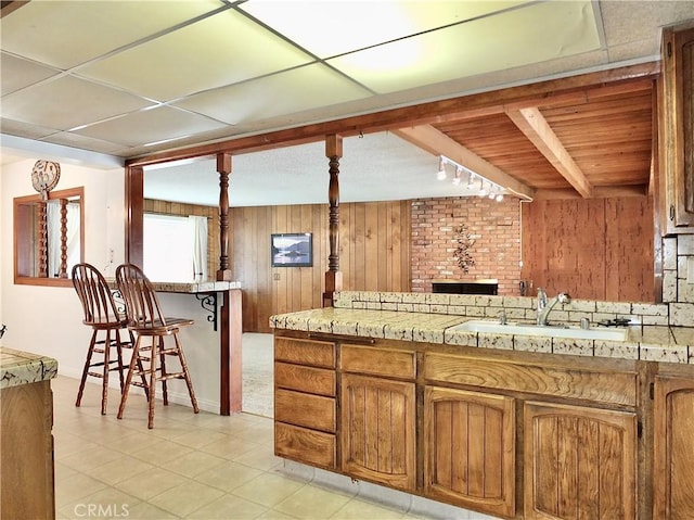 kitchen featuring wooden walls, a sink, light countertops, a kitchen bar, and beamed ceiling