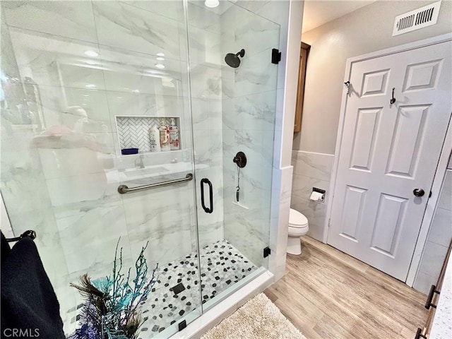 bathroom featuring toilet, wood finished floors, visible vents, tile walls, and a shower stall