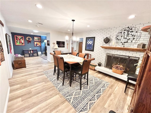 dining room featuring a notable chandelier, light wood finished floors, recessed lighting, a brick fireplace, and brick wall