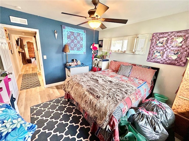 bedroom with a ceiling fan, visible vents, baseboards, and wood finished floors