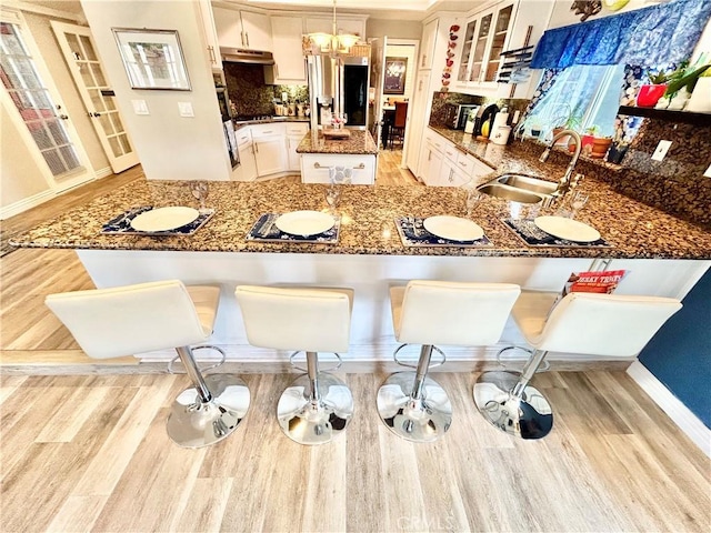 kitchen featuring a center island, glass insert cabinets, a sink, dark stone counters, and stainless steel fridge with ice dispenser