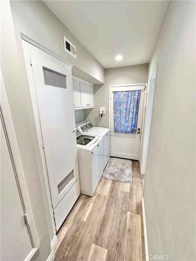 clothes washing area with visible vents, cabinet space, light wood-style flooring, and separate washer and dryer