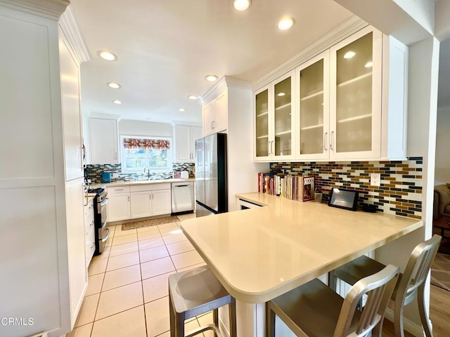 kitchen featuring light tile patterned flooring, stainless steel appliances, a peninsula, a sink, and light countertops