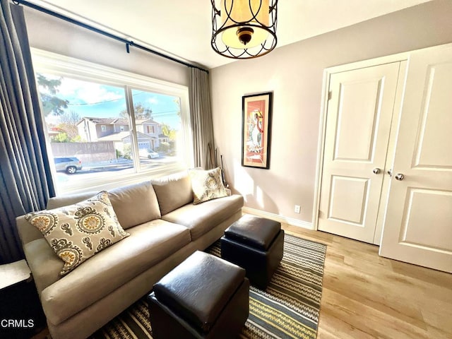 living area featuring a notable chandelier, light wood finished floors, and baseboards