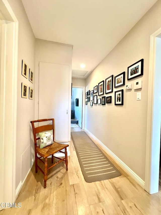 hallway featuring attic access, light wood-style flooring, and baseboards