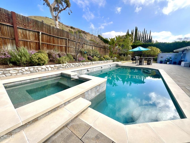 view of swimming pool featuring a patio area, a fenced backyard, a fenced in pool, and an in ground hot tub