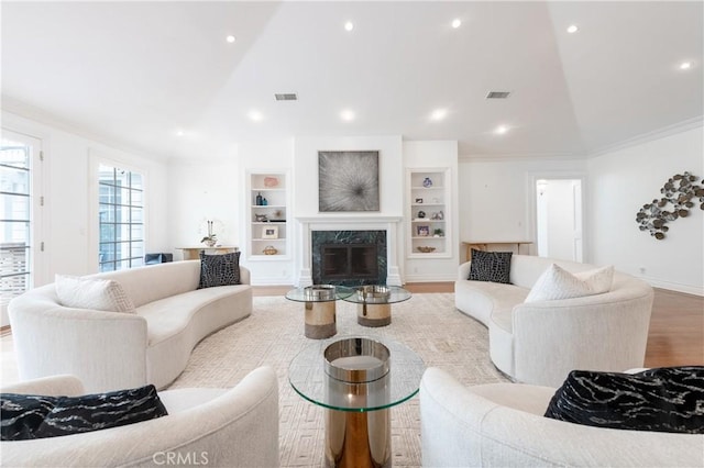 living area with built in shelves, crown molding, visible vents, a high end fireplace, and wood finished floors