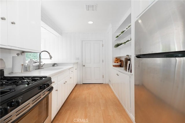 kitchen featuring light wood finished floors, visible vents, white cabinets, gas range, and a sink