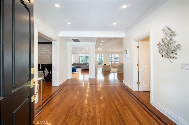 hall featuring baseboards, crown molding, visible vents, and wood finished floors