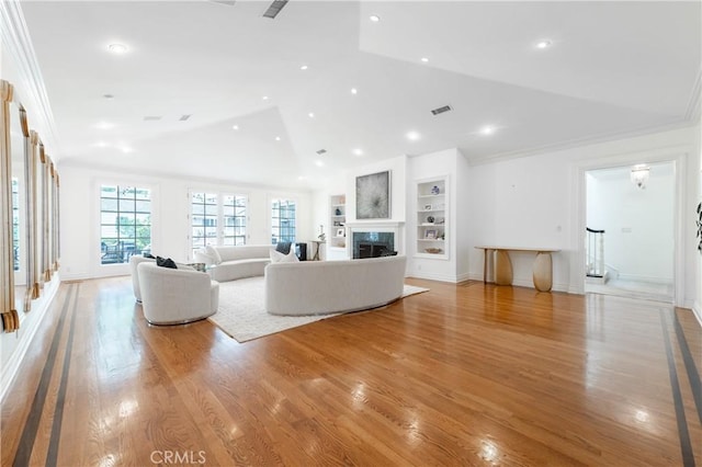 unfurnished living room featuring built in shelves, a fireplace, ornamental molding, vaulted ceiling, and light wood-type flooring