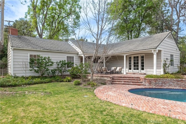 back of property with a chimney, an outdoor pool, a patio, and a yard