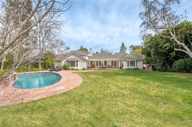 back of property with a yard, a chimney, a patio area, and an outdoor pool