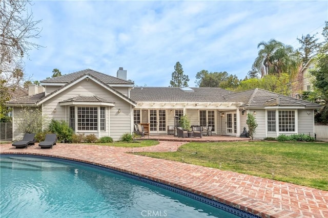 back of property featuring a patio, french doors, a lawn, an outdoor pool, and a chimney