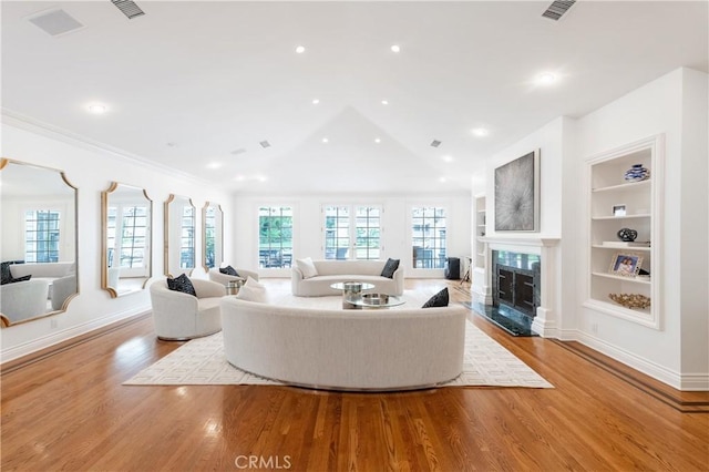 living area with lofted ceiling, built in shelves, a premium fireplace, wood finished floors, and baseboards