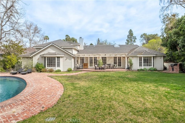 back of property featuring a yard, a chimney, an outdoor pool, and a patio