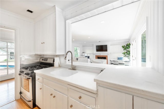 kitchen featuring a fireplace, light countertops, light wood-style floors, a sink, and stainless steel gas range