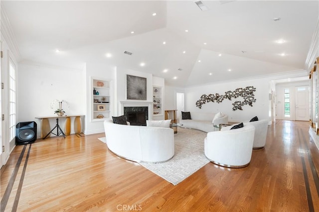 living room with visible vents, built in features, a premium fireplace, ornamental molding, and light wood-type flooring