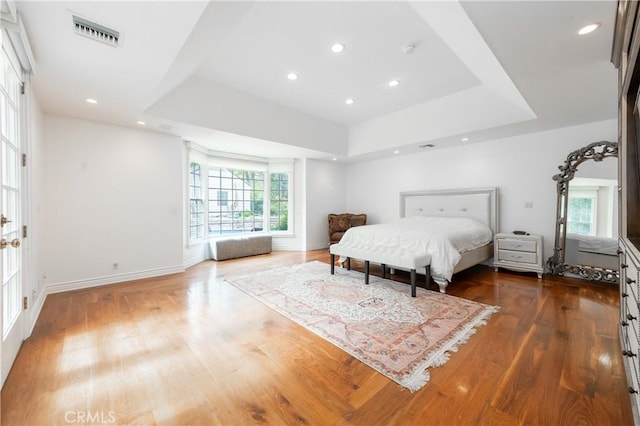 bedroom featuring wood finished floors, a raised ceiling, visible vents, and baseboards