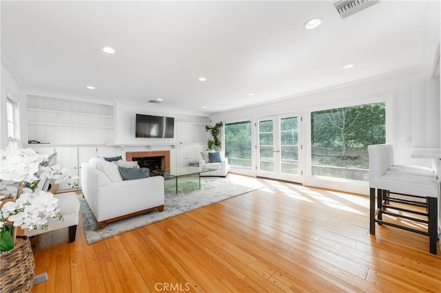 living area with ornamental molding, hardwood / wood-style floors, a fireplace, and visible vents