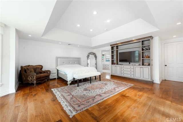 bedroom featuring baseboards, a raised ceiling, wood finished floors, and recessed lighting