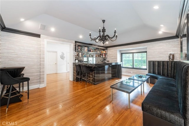 living area with lofted ceiling, bar area, ornamental molding, light wood-type flooring, and a tray ceiling