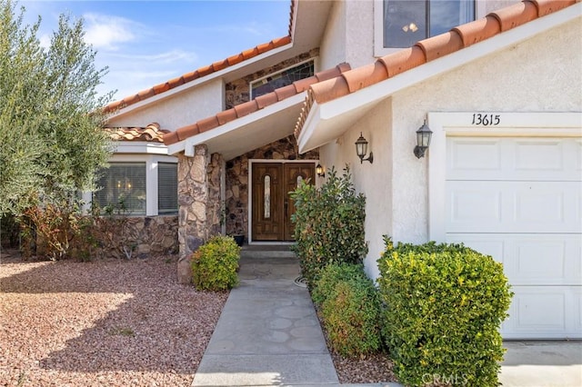 view of exterior entry featuring a garage, stone siding, a tile roof, and stucco siding