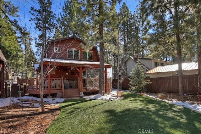 back of property with a yard, a standing seam roof, metal roof, fence, and a wooden deck