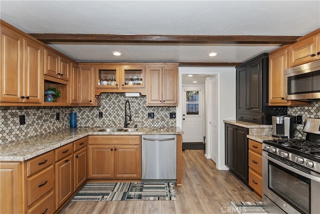 kitchen featuring light wood finished floors, appliances with stainless steel finishes, a sink, and beam ceiling