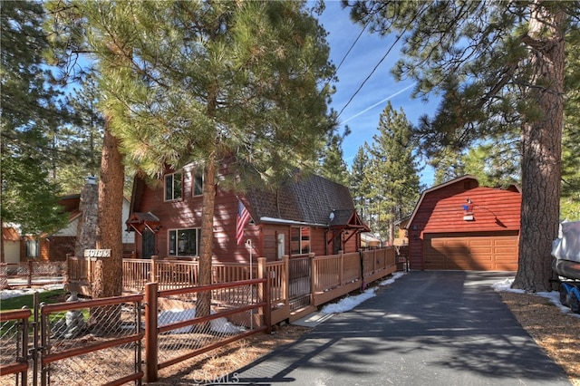 view of front of home featuring a shingled roof, a detached garage, an outdoor structure, and fence