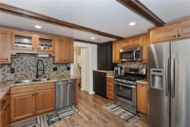 kitchen with light stone counters, wood finished floors, a sink, appliances with stainless steel finishes, and beam ceiling