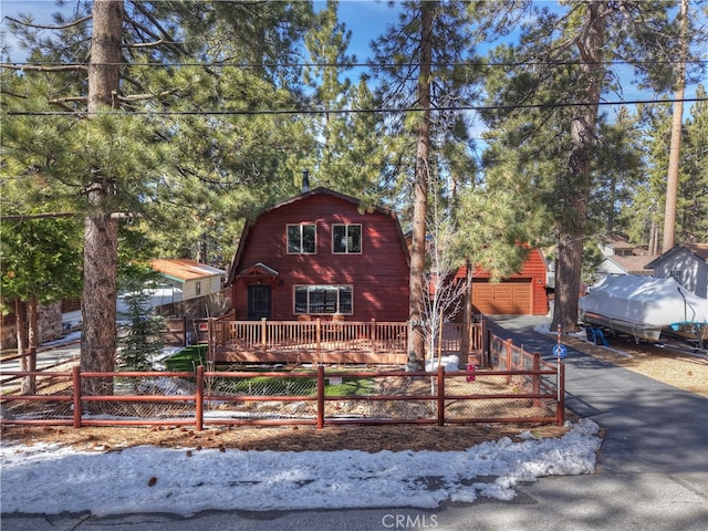 view of front facade with a fenced front yard, an outdoor structure, driveway, and a gambrel roof