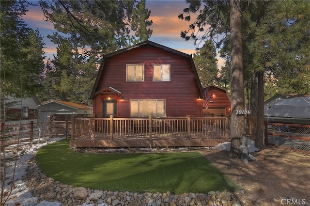 back of house at dusk with a deck, a yard, fence, and a gambrel roof