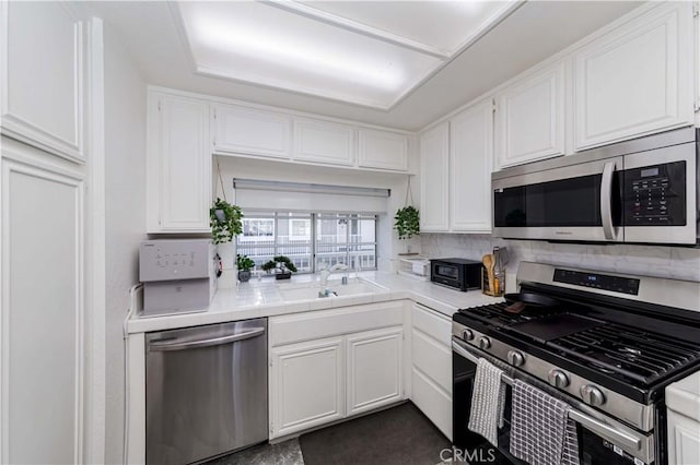 kitchen featuring stainless steel appliances, tile counters, white cabinets, and a sink