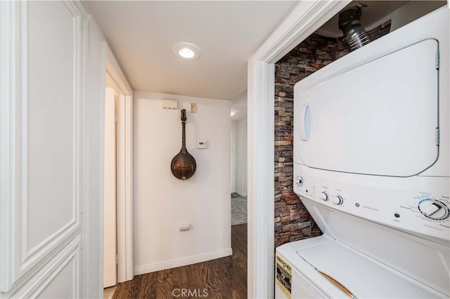 washroom featuring stacked washer / dryer, laundry area, baseboards, and wood finished floors