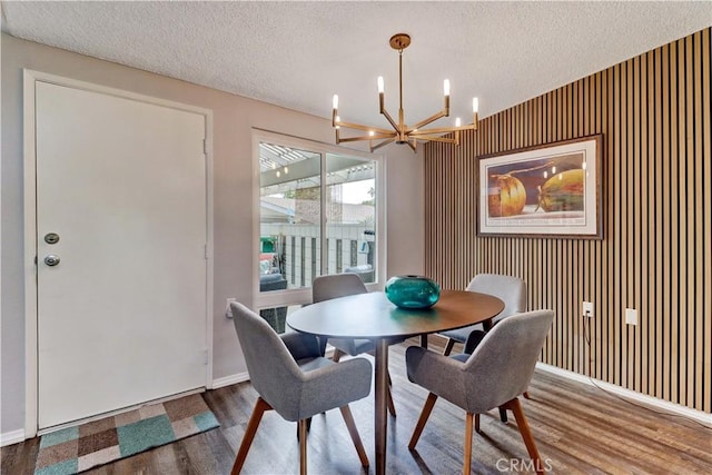 dining space featuring a chandelier, a textured ceiling, wood finished floors, and baseboards