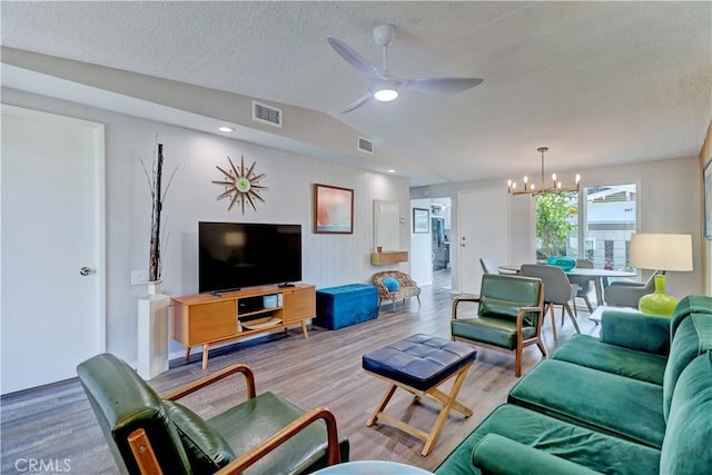 living room with lofted ceiling, visible vents, wood finished floors, and ceiling fan with notable chandelier