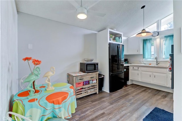 kitchen with white cabinets, vaulted ceiling, a sink, wood finished floors, and black appliances