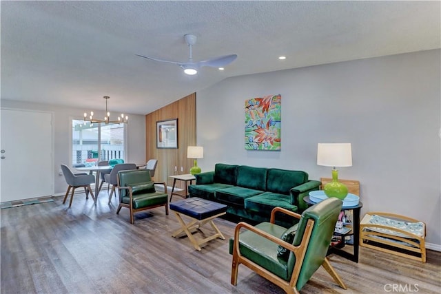 living area with ceiling fan with notable chandelier, vaulted ceiling, a textured ceiling, and wood finished floors