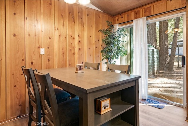 dining room featuring lofted ceiling, wood walls, and wood finished floors