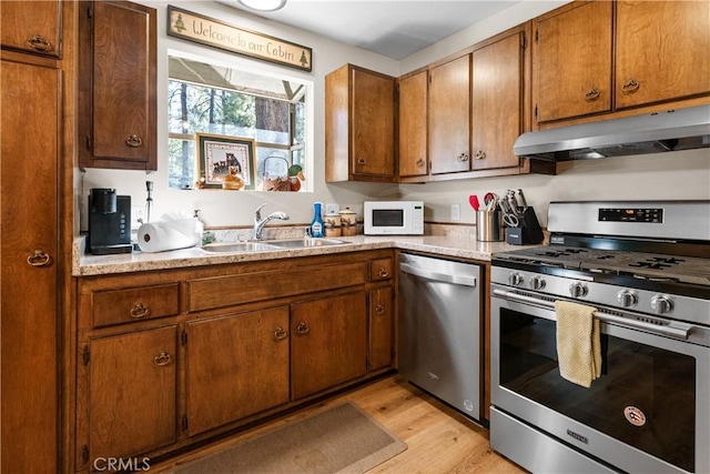 kitchen featuring under cabinet range hood, appliances with stainless steel finishes, light countertops, and a sink