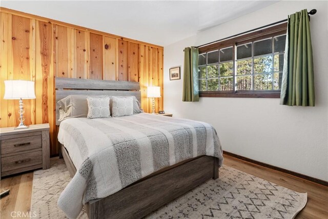 bedroom with wood walls, baseboards, and wood finished floors