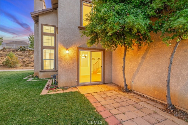 exterior entry at dusk with a lawn, a patio, and stucco siding